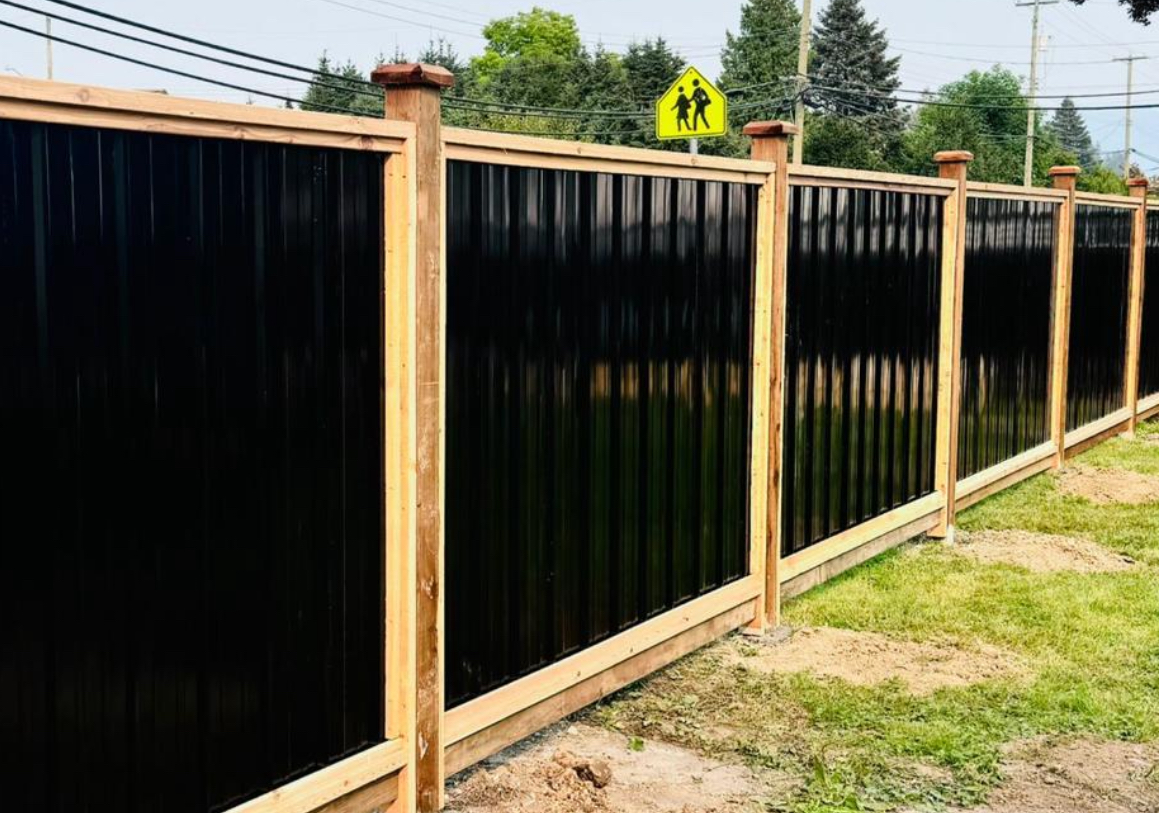 Black corrugated metal privacy fence with cedar posts and rails along a roadside