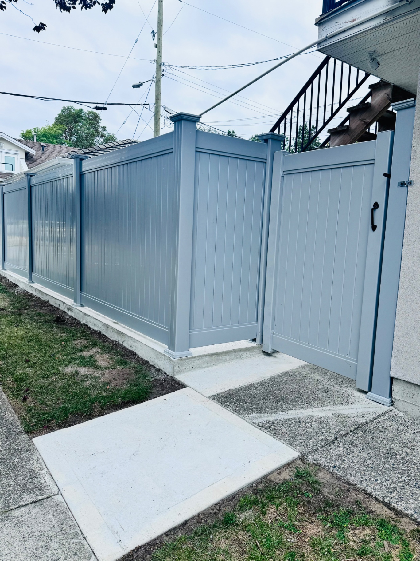 Grey vinyl privacy fence with a matching swing gate along a concrete walkway